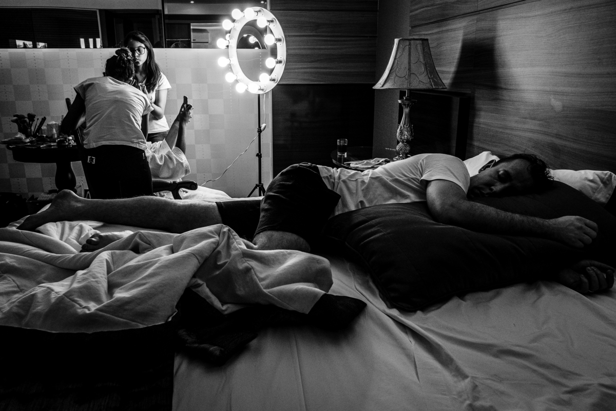 noiva se maquiando enquanto padrinho cochila no making of