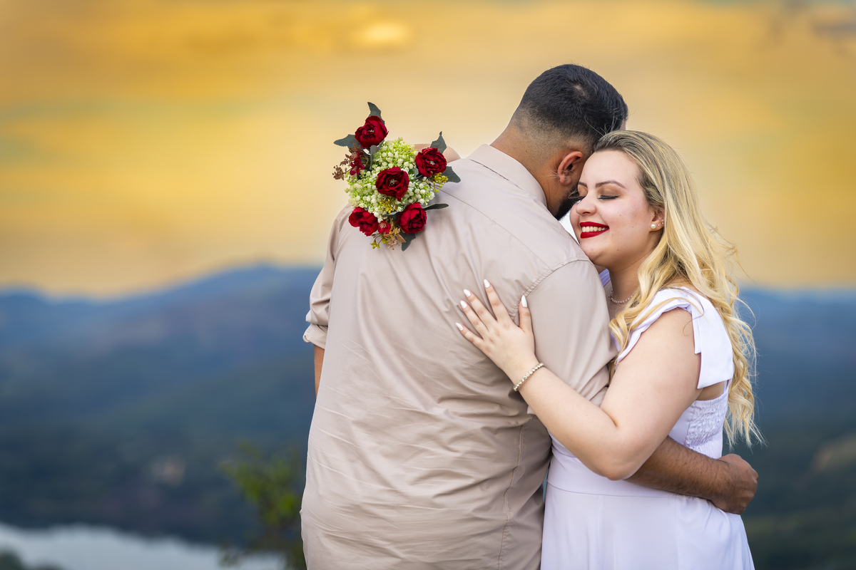 No alto do Morro do Capuava, Kamila e Daniel contemplam o amor que os eleva — tão leve quanto o voo ao fundo., ensaio pré-wedding Alphaville, ensaio fotográfico pré-wedding Morro do Capuava ensaio, fotos de casal ao pôr do sol, pré-wedding com parapente