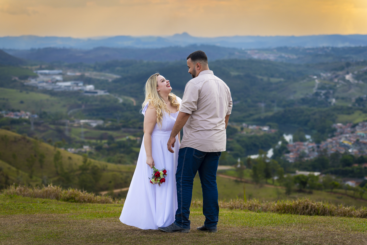No alto do Morro do Capuava, Kamila e Daniel contemplam o amor que os eleva — tão leve quanto o voo ao fundo., ensaio pré-wedding Alphaville, ensaio fotográfico pré-wedding Morro do Capuava ensaio, fotos de casal ao pôr do sol, pré-wedding com parapente