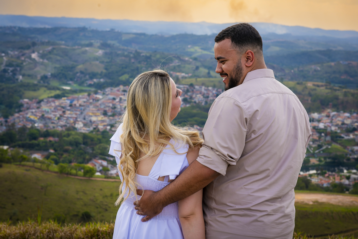 No alto do Morro do Capuava, Kamila e Daniel contemplam o amor que os eleva — tão leve quanto o voo ao fundo., ensaio pré-wedding Alphaville, ensaio fotográfico pré-wedding Morro do Capuava ensaio, fotos de casal ao pôr do sol, pré-wedding com parapente