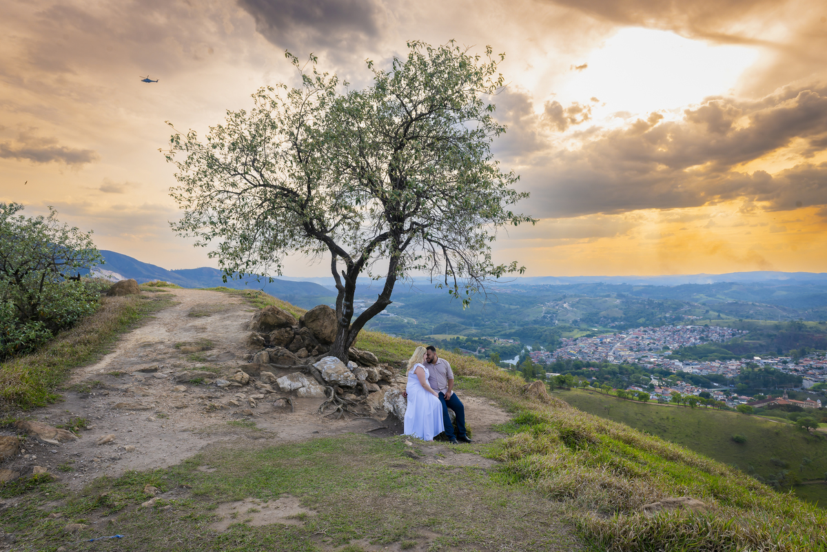 No alto do Morro do Capuava, Kamila e Daniel contemplam o amor que os eleva — tão leve quanto o voo ao fundo., ensaio pré-wedding Alphaville, ensaio fotográfico pré-wedding Morro do Capuava ensaio, fotos de casal ao pôr do sol, pré-wedding com parapente