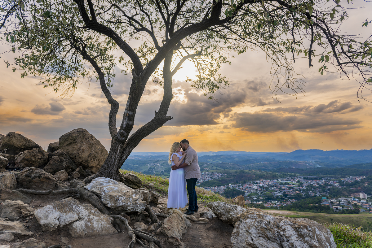 No alto do Morro do Capuava, Kamila e Daniel contemplam o amor que os eleva — tão leve quanto o voo ao fundo., ensaio pré-wedding Alphaville, ensaio fotográfico pré-wedding Morro do Capuava ensaio, fotos de casal ao pôr do sol, pré-wedding com parapente