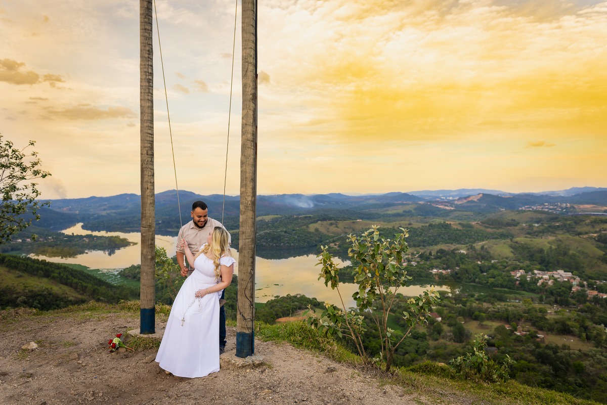 No alto do Morro do Capuava, Kamila e Daniel contemplam o amor que os eleva — tão leve quanto o voo ao fundo., ensaio pré-wedding Alphaville, ensaio fotográfico pré-wedding Morro do Capuava ensaio, fotos de casal ao pôr do sol, pré-wedding com parapente