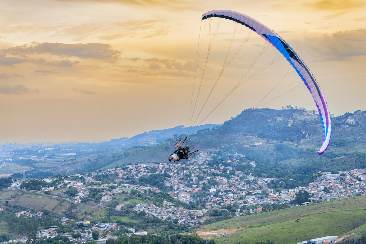 No alto do Morro do Capuava, Kamila e Daniel contemplam o amor que os eleva — tão leve quanto o voo ao fundo., ensaio pré-wedding Alphaville, ensaio fotográfico pré-wedding Morro do Capuava ensaio, fotos de casal ao pôr do sol, pré-wedding com parapente