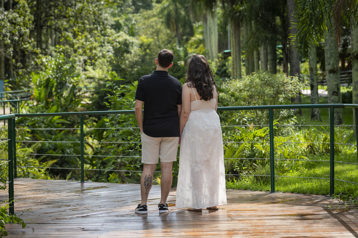 Casal de noivos de costas, de mãos dadas, contemplando a mata densa do Jardim Botânico de São Paulo em ensaio pré-wedding.
