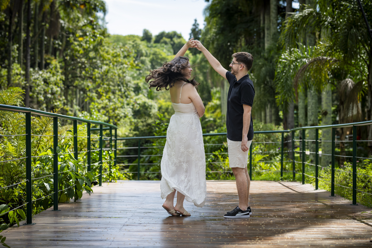 Momento de dança e giro do casal de noivos sobre passarela de madeira, cabelo ao vento, durante ensaio pré-wedding no Jardim Botânico de SP.