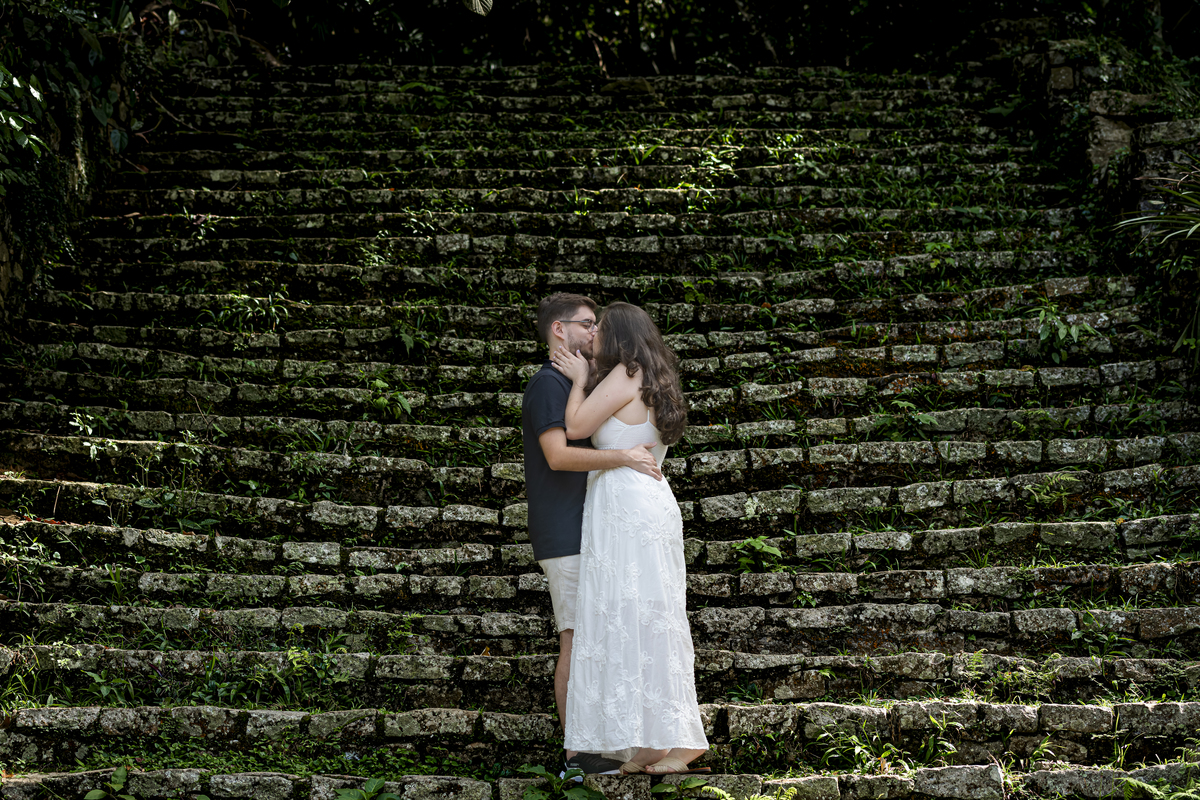 Beijo romântico do casal em frente à escadaria histórica de pedra coberta de musgo no Jardim Botânico de São Paulo.
