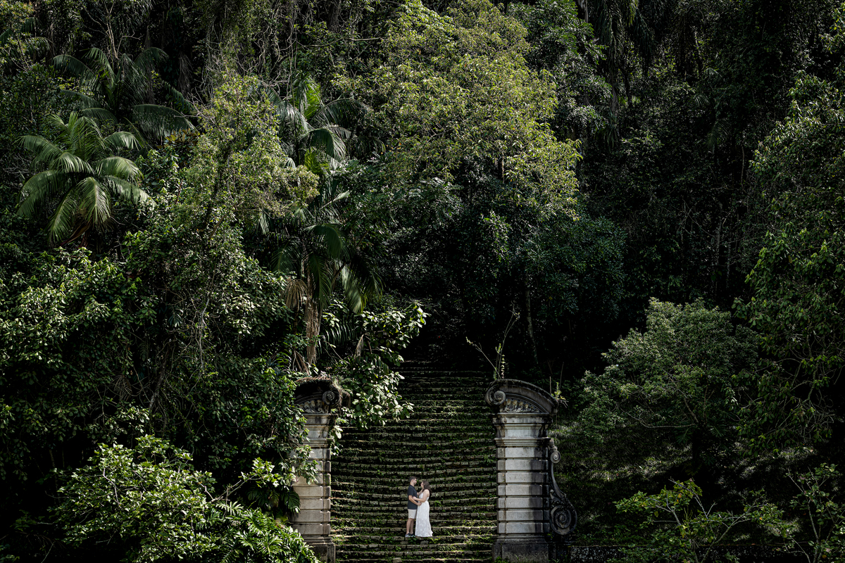 Vista aérea da icônica escadaria de pedra do Jardim Botânico de São Paulo, com o casal de noivos pequeno em meio à imensidão verde da mata.