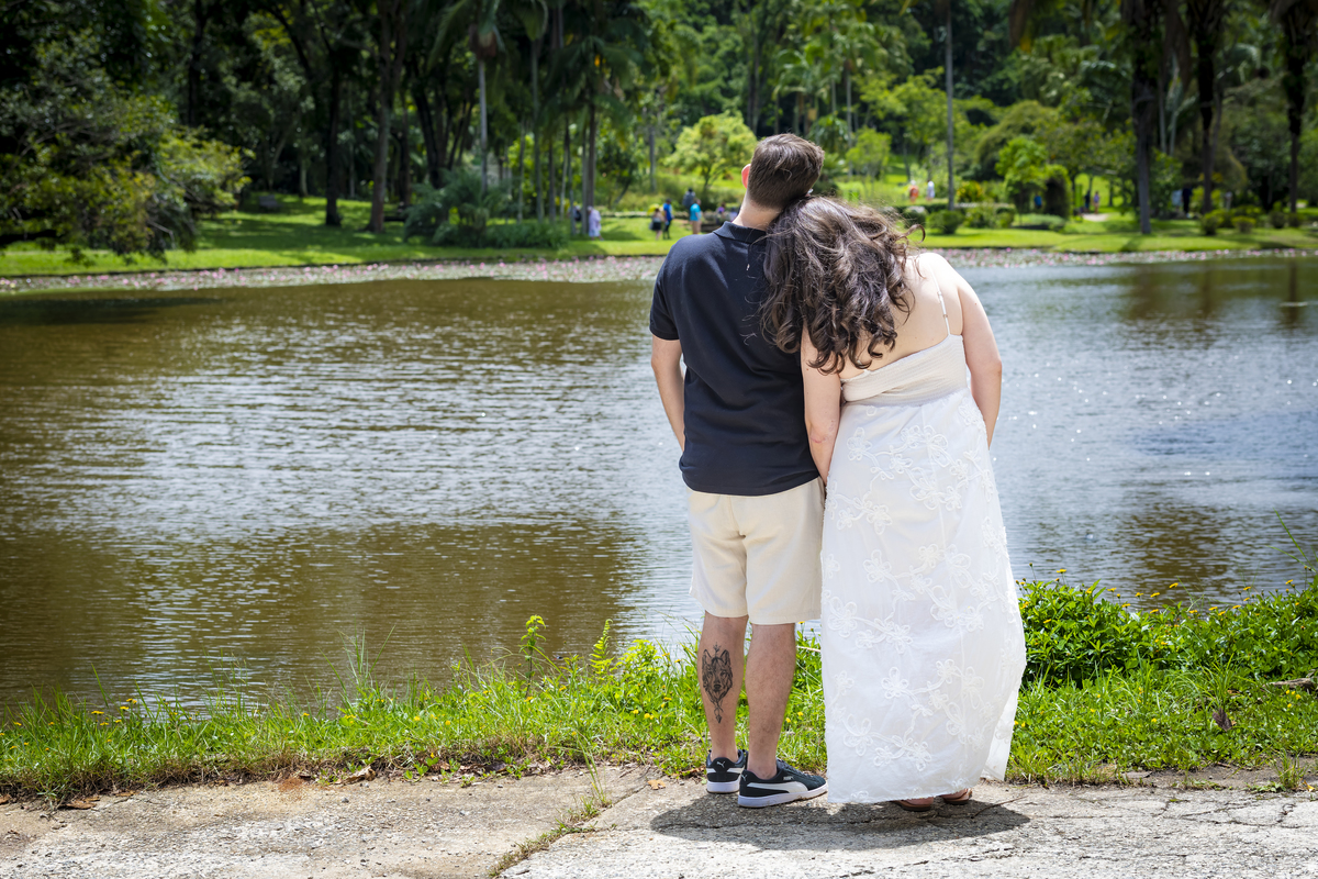 Casal de noivos de costas, abraçados, observando o lago principal do Jardim Botânico de São Paulo.