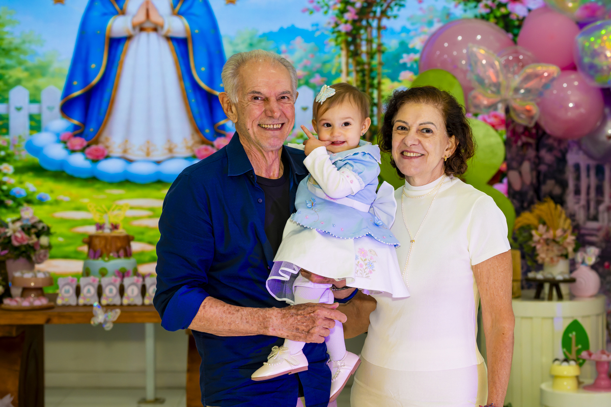 Os avós posando com a aniversariante no colo, diante da decoração azul e rosa da festa.