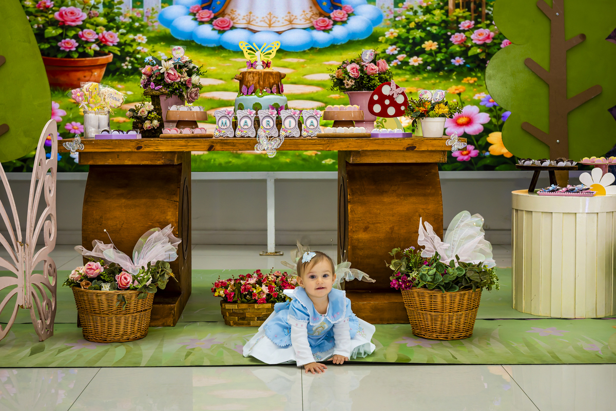 A aniversariante engatinhando pelo espaço decorado, cercada por cestos de flores e elementos do tema jardim.
