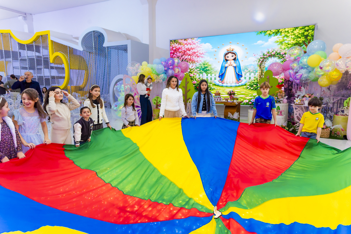 Grupo de crianças segura paraquedas colorido para brincadeira em festa infantil no buffet Lá Vem o Sol - Lua.