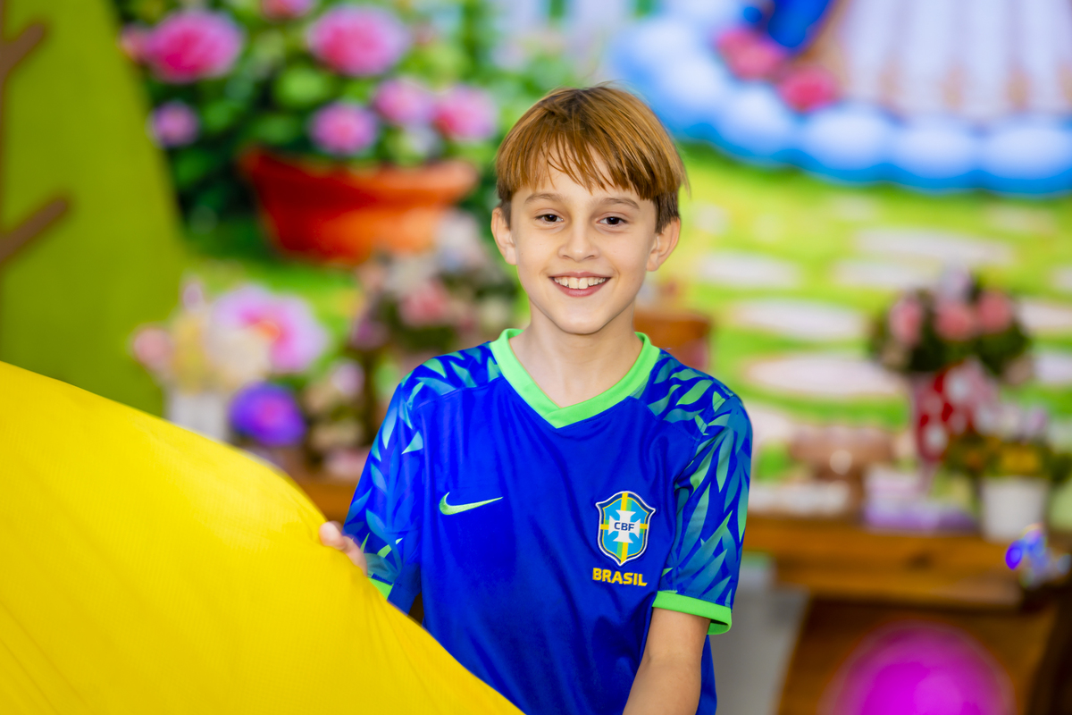 Convidado sorridente com camisa da seleção brasileira posa em cenário de jardim na festa de aniversário.