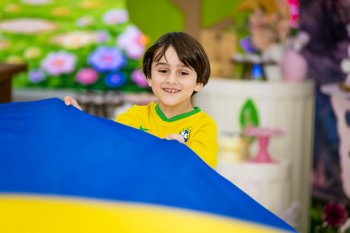 Criança segura tecido azul do paraquedas colorido durante brincadeira na festa infantil em Alphaville.