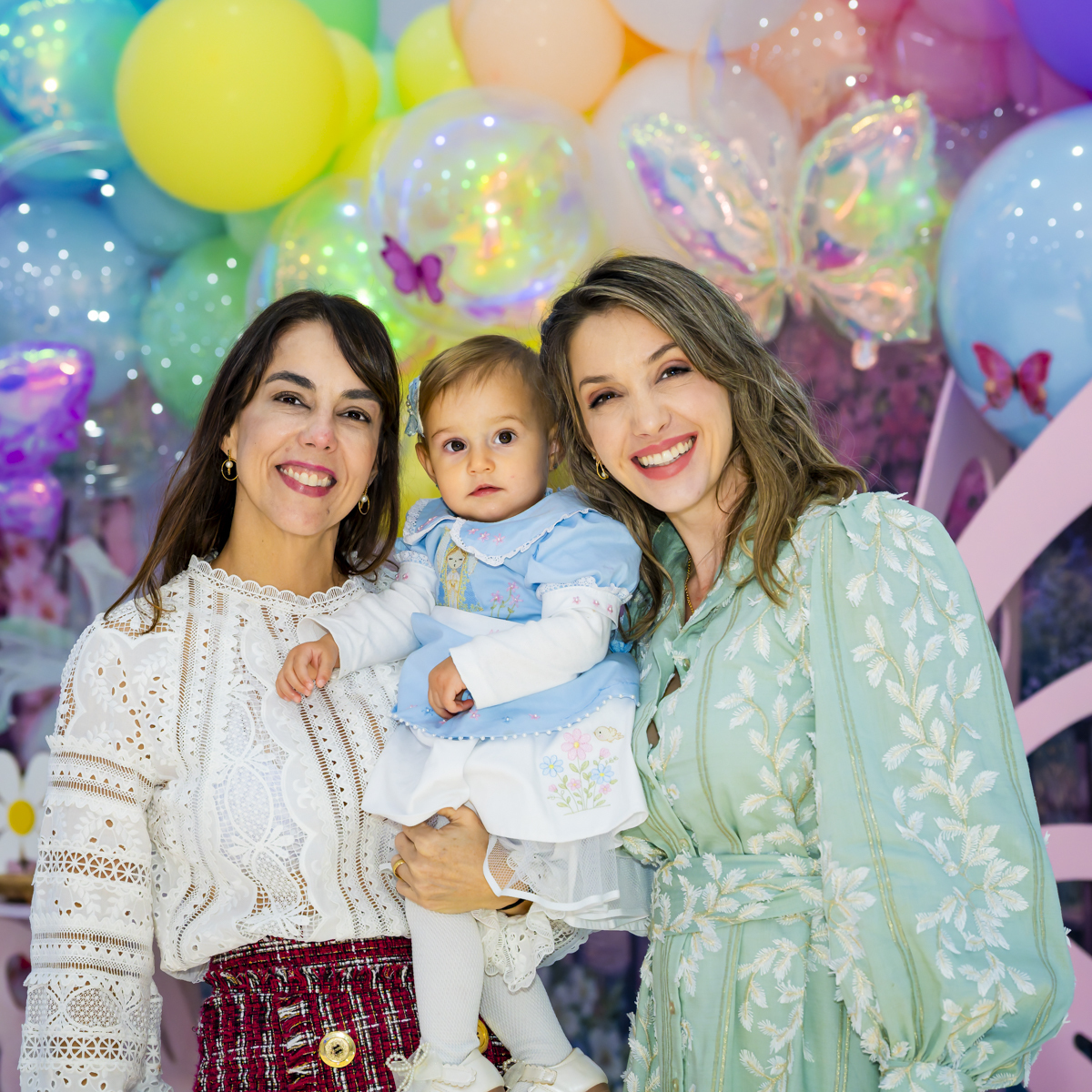 Madrinha e mão sorriem ao lado da aniversariante, cercadas por arranjo de balões coloridos com borboletas, no espaço de festas Lá Vem o Sol - Lua.