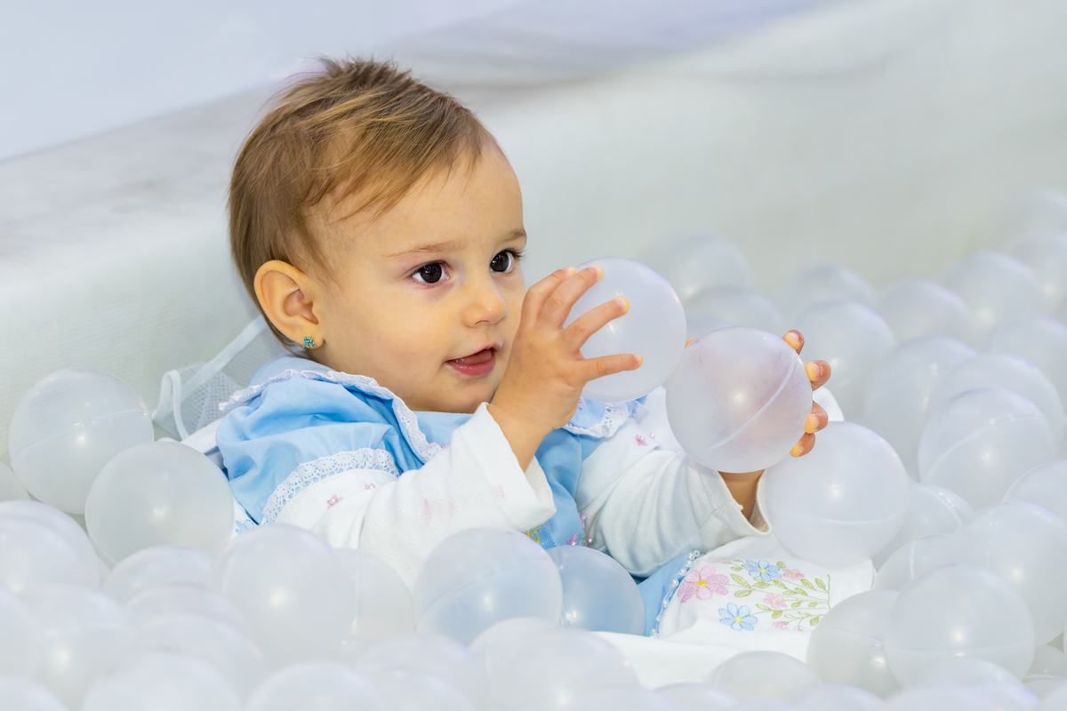 Bebê aniversariante brinca atenta com bolinhas brancas dentro da piscina de bolinhas, um dos destaques do espaço infantil Lá Vem o Sol - Lua.