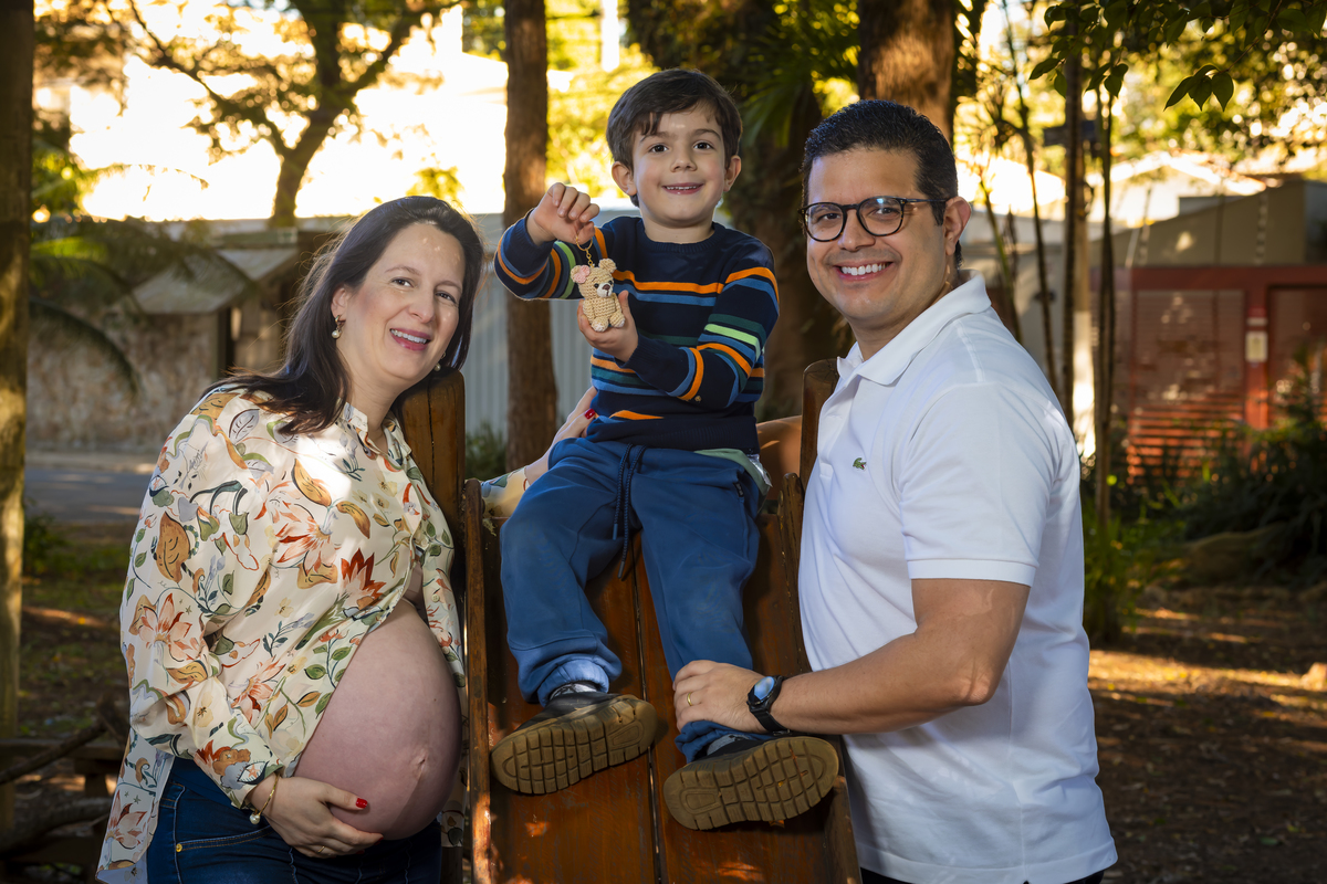 Família completa sorri junta no playground da praça Conde Barcelos em São Paulo, o filho segura um ursinho de crochê, encerrando o ensaio com carinho e leveza.