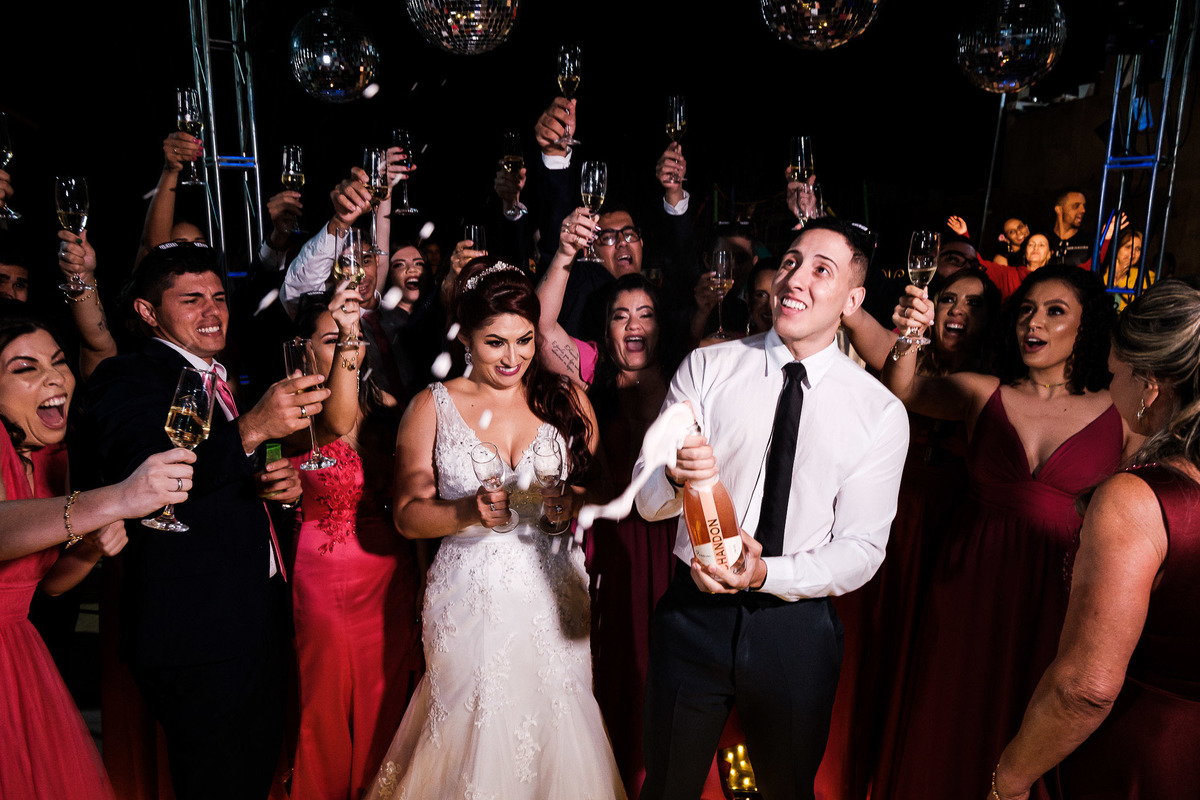 casal estourando o champanhe com os convidados e padrinhos
