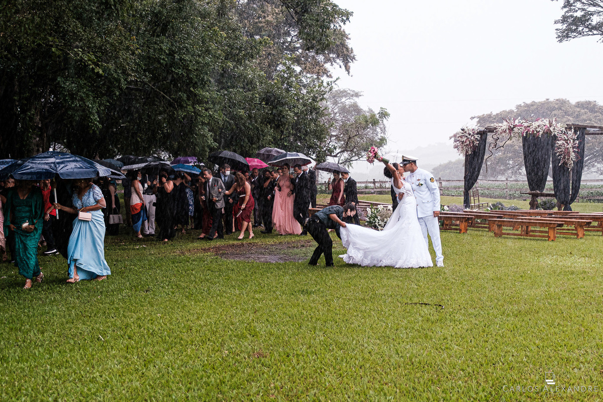 noivos se beijando debaixo de chuva enquanto os convidados se molham