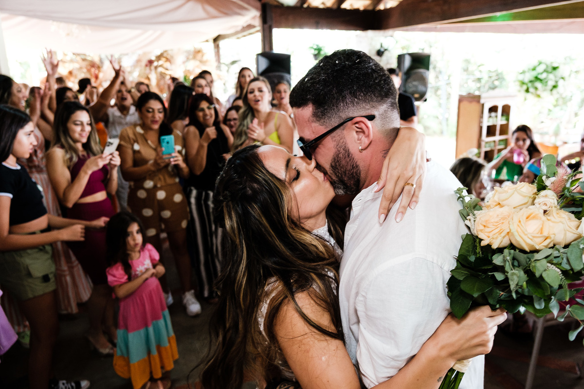 noivos se beijando com família comemorando ao fundo