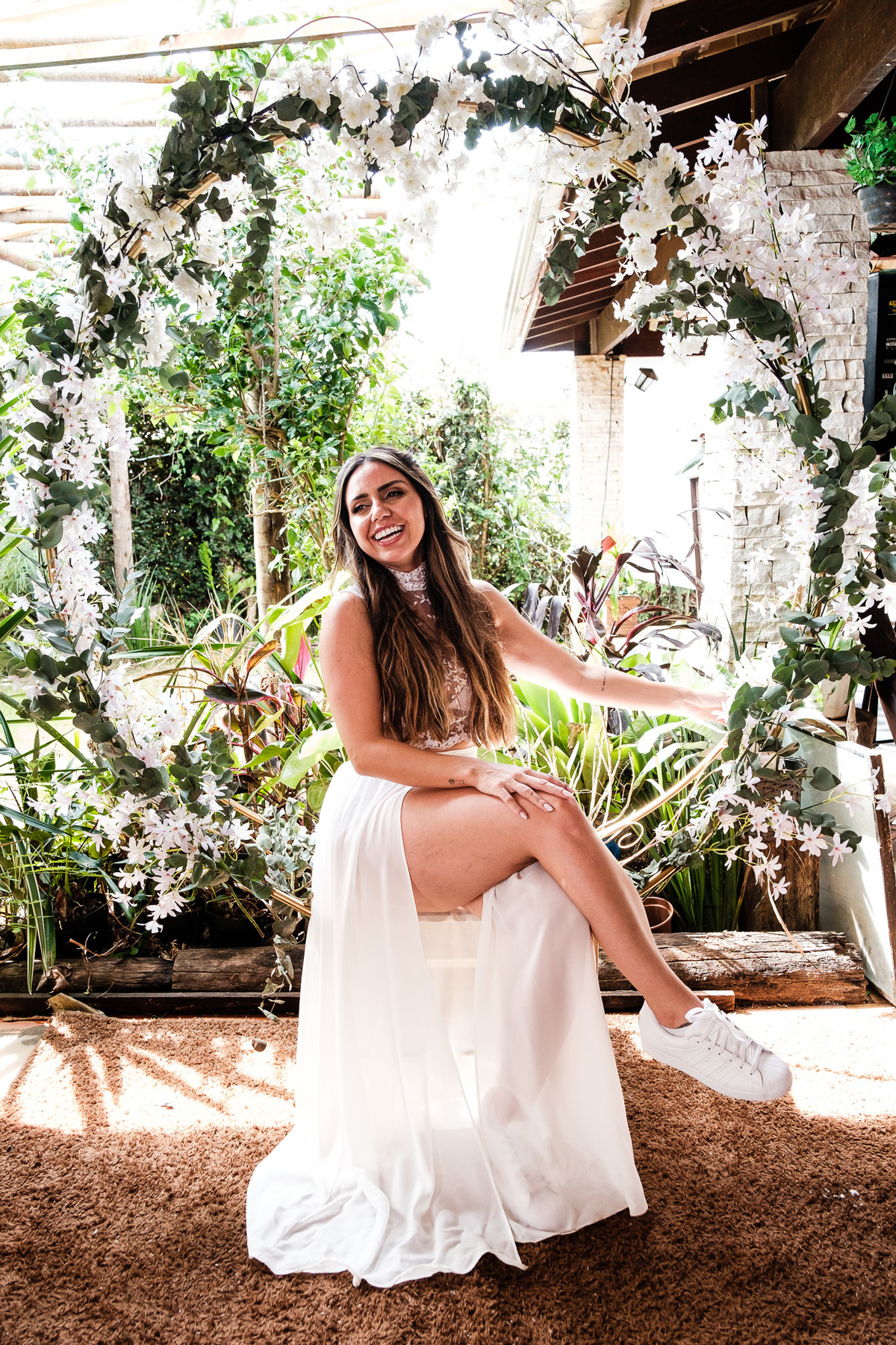 noiva sentado com arco de flores ao fundo mostrando suas pernas