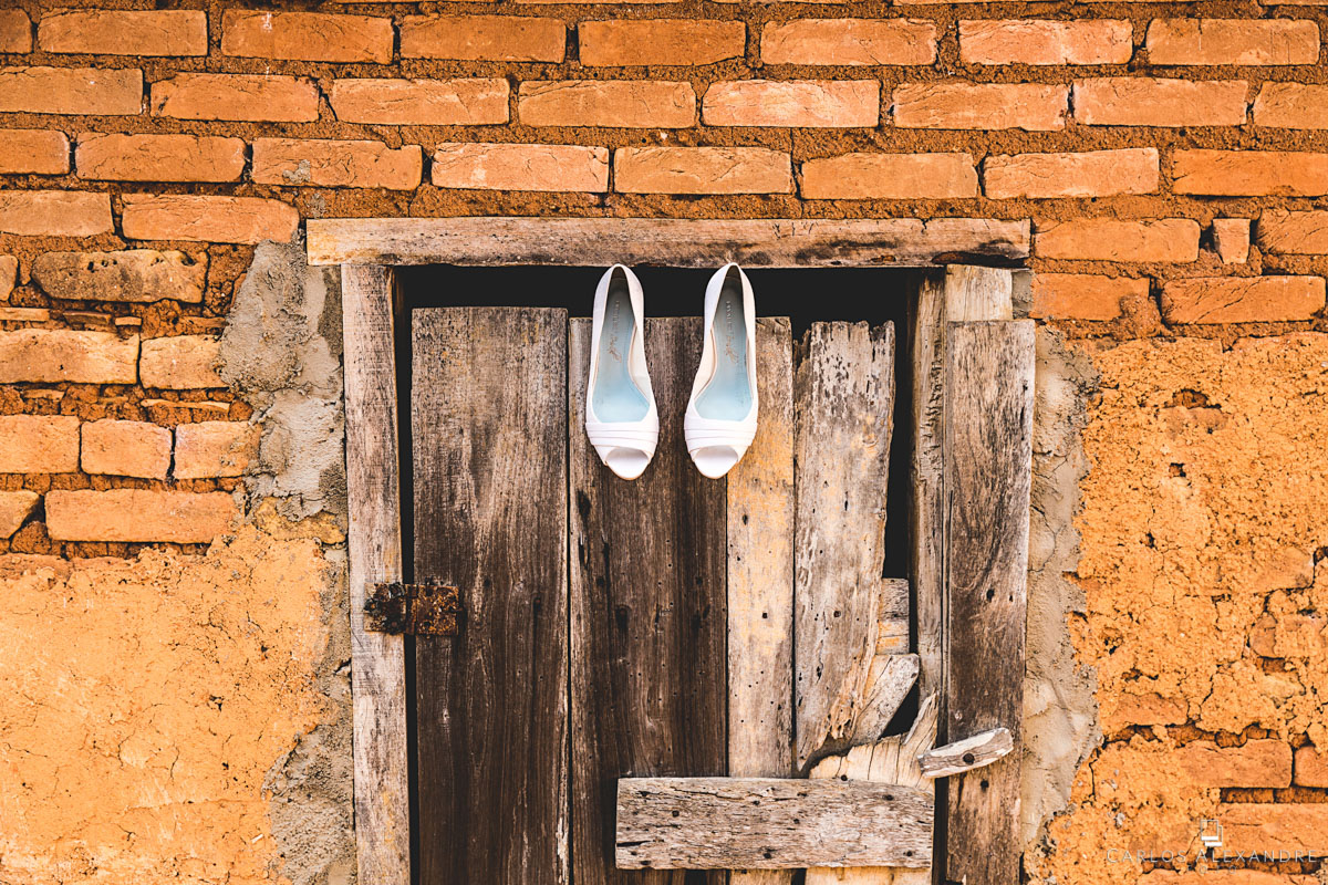 sapatos da noiva pendurados em uma porta com tijolos fotografado por carlos alexandre foto fotógrafo em três corações sul de minas