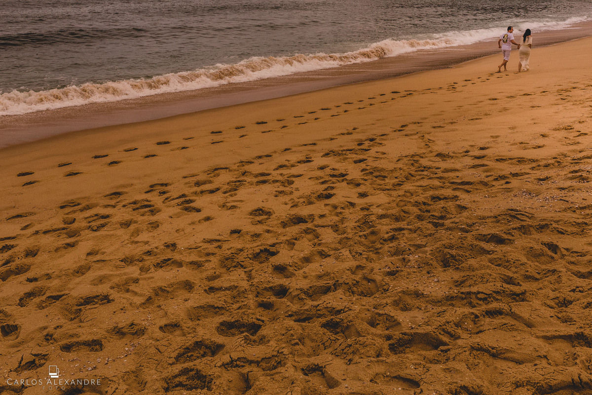 duas pessoas que se amam correndo com pegadas na areia rente ao mar, indo em direção ao seu destino