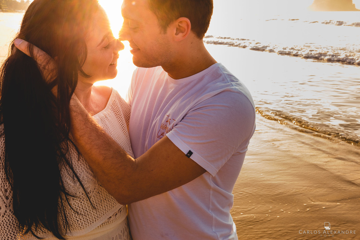 marido agarrando os cabelos de sua esposa, à luz amarelada do sol que acaba de nascer, com o oceano ao fundo
