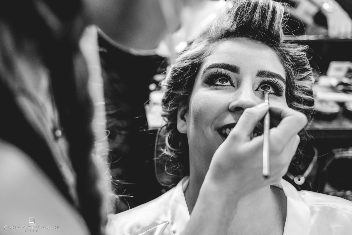 bela noiva se maquiando com um lindo sorriso antes de seu casamento, no salão, fotógrafo de casamentos Carlos Alexandre Fotografia Três Corações MG