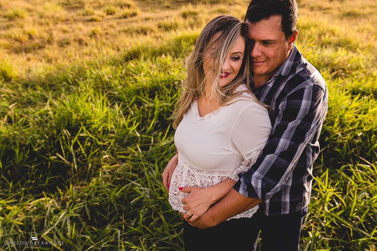 papais se abraçando e esperando a vinda da pequena nina dentro da barriga da mãe, no ensaio de gestante em três corações carlos alexandre foto