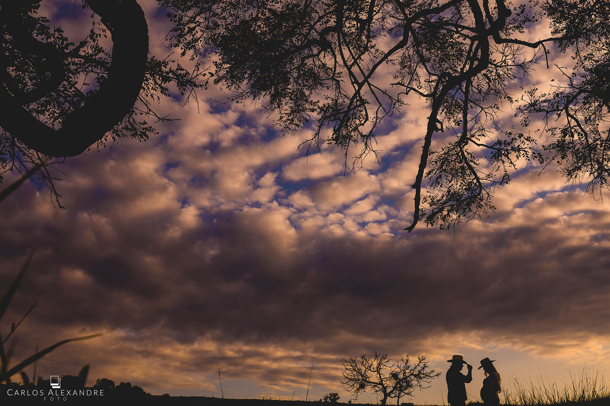 contra luz de casal country durante ensaio de gestante, usando chapéu caip, no ensaio de gestante em três corações carlos alexandre foto