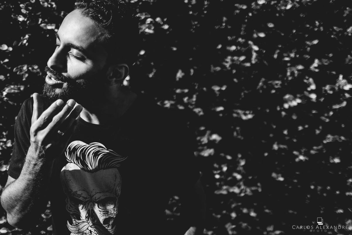 homem passando a mão na barba, com sua camisa preta com estampa de caveira, fazendo biquinho