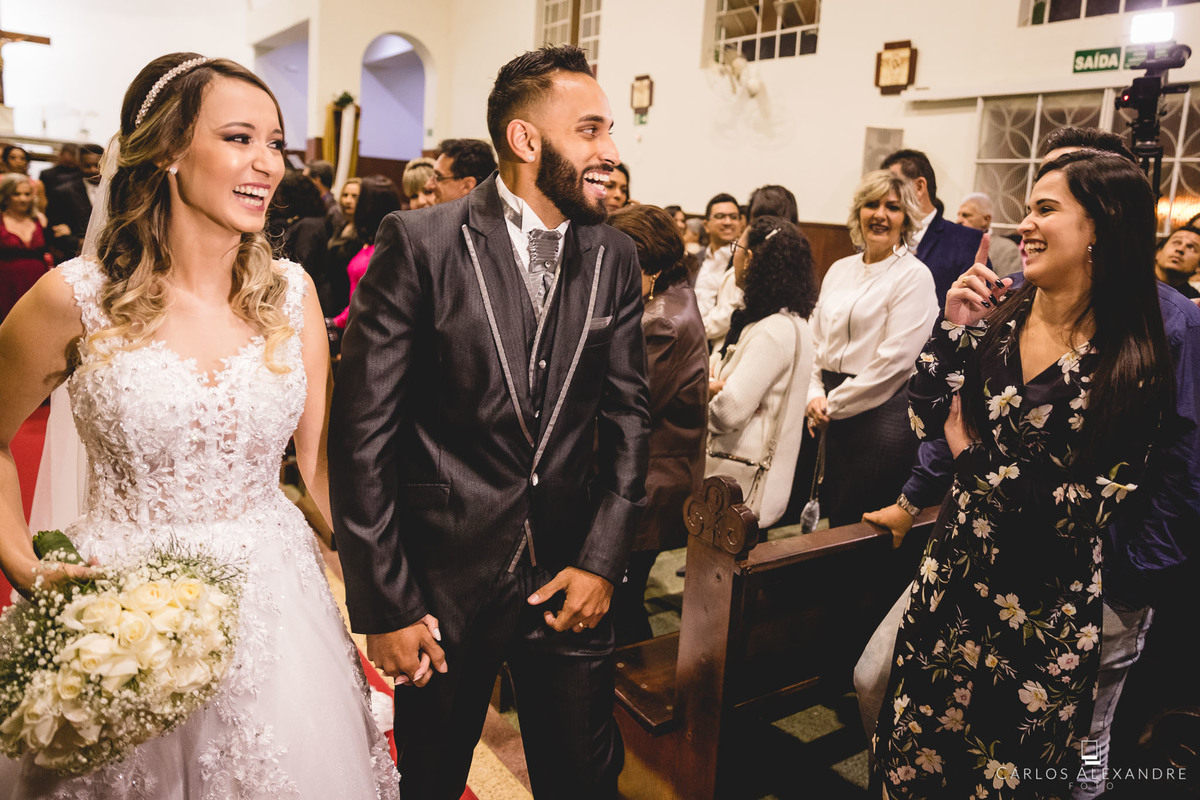 noivos cumprimentam convidados sorrindo a beça enquanto saem da igreja
