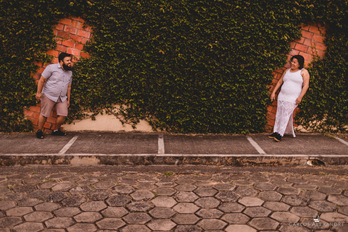 casam se olhando e admirando, em um morro com uma parede viva, com dois espaços com tijolos, fotos de gordinhos pre wedding carlos alexandre fotografo de casamento
