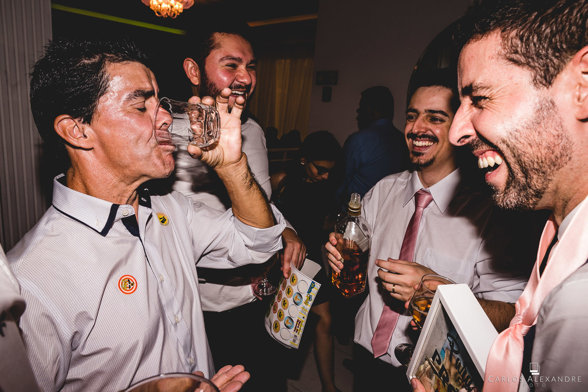 convidado virando copo de whyski enquanto noivo da gargalhadas, festa do casamento no salão boa vista em pouso alegre, fotógrafo de casamentos carlos alexandre de três corações mg sul de minas