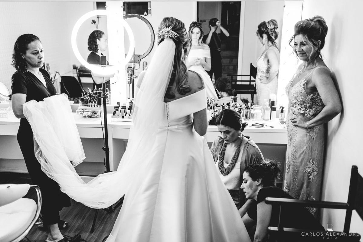 noiva e sua mãe, junto com as meninas do salão finalizando os detalhes após colocarem o vestido, making of da noiva no salão de mariana loyola, fotografado por carlos alexandre fotógrafo de três corações mg