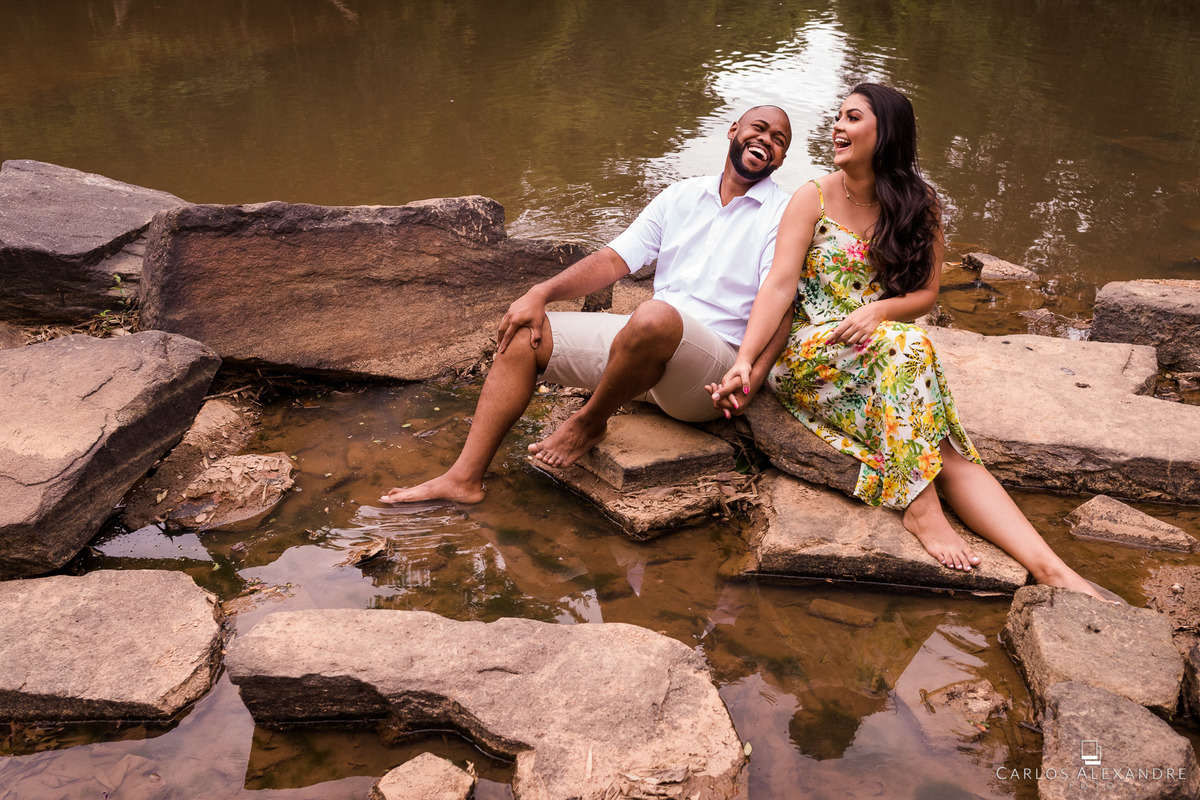ensaio de casal  pré wedding na beira do rio no recanto da família em três corações mg carlos alexandre foto casal namorando e sorrindo sentados nas pedras na beira de um pequno ribeirão