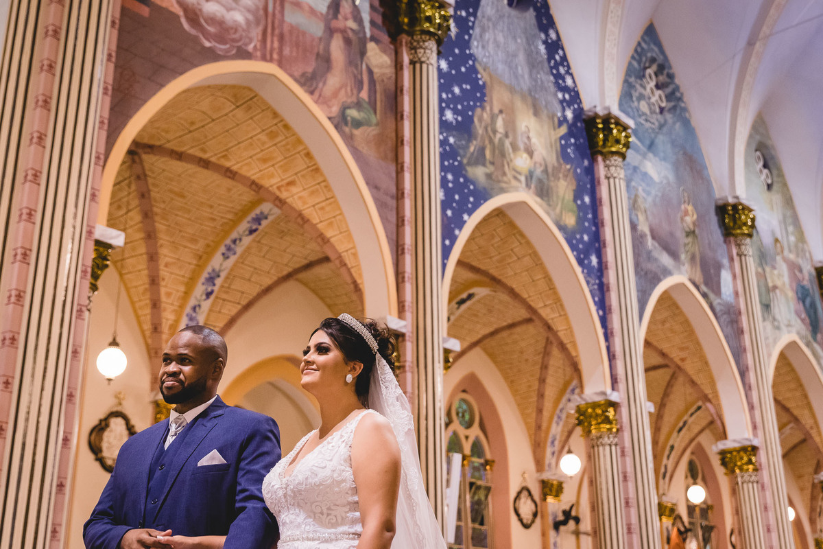 cerimônia de casamento na igreja matriz de três corações mg carlos alexandre fotógrafo casal com as paredes da igreja ao fundo, com as pinturas de passagens bíblicas na matriz reformada