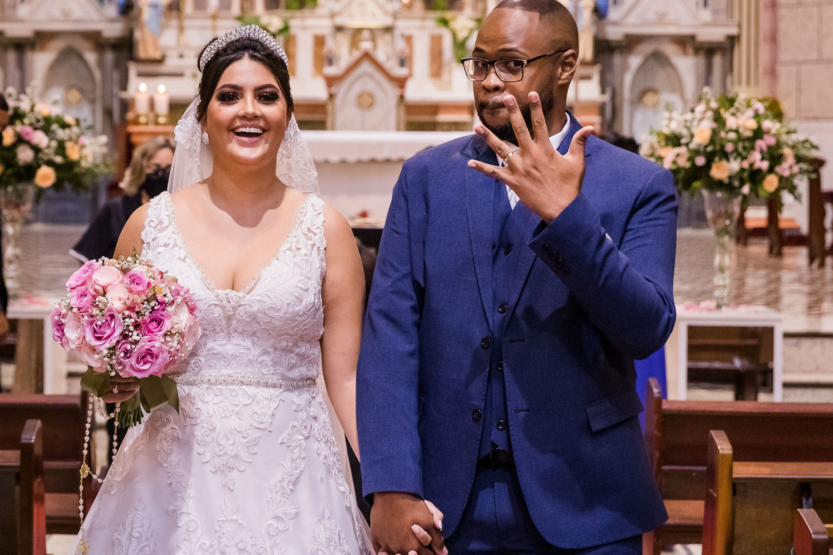 cerimônia de casamento na igreja matriz de três corações mg carlos alexandre fotógrafo noivos recém casados saindo da igreja e fazendo gracinha mostrando sua aliança na mão esquerda