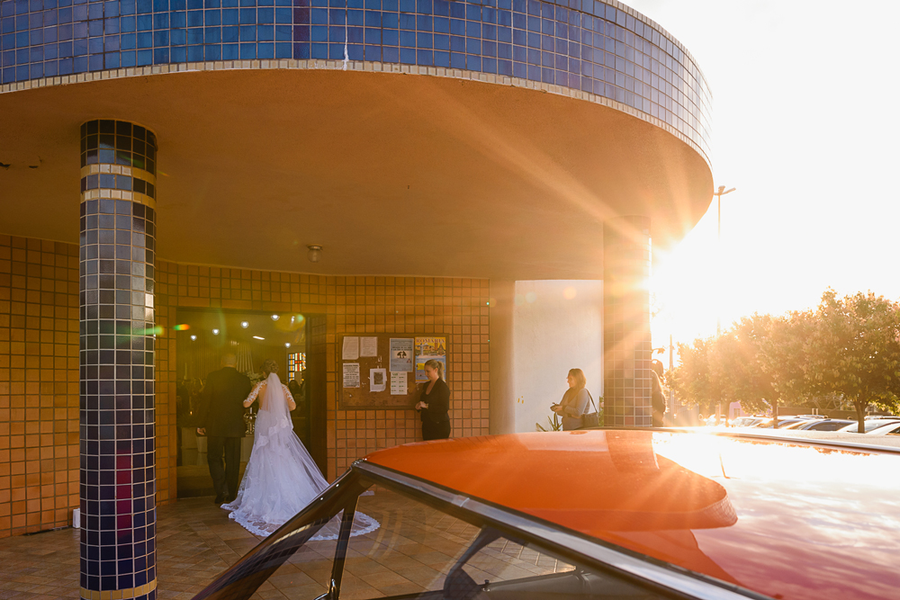 Foto da noiva na porta da igreja com o por do sol e o Opala vermelho na porta