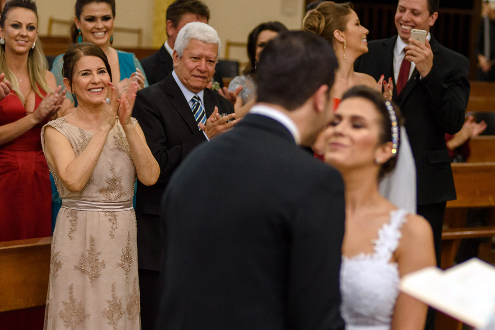 Família do noivo em segundo plano aplaudindo enquanto eles se beijam