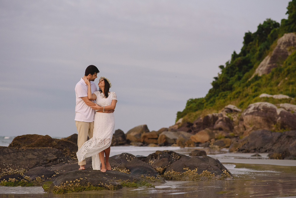 Foto dos noivos na beira da praia em cima das pedras