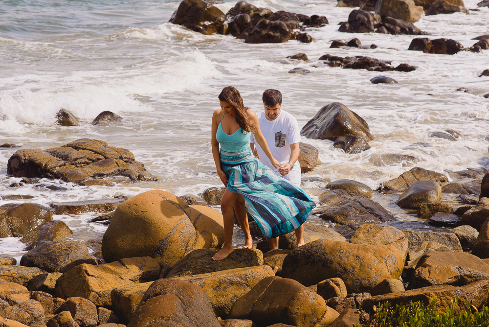 Noivos caminhando por cima das pedras na beira da praia