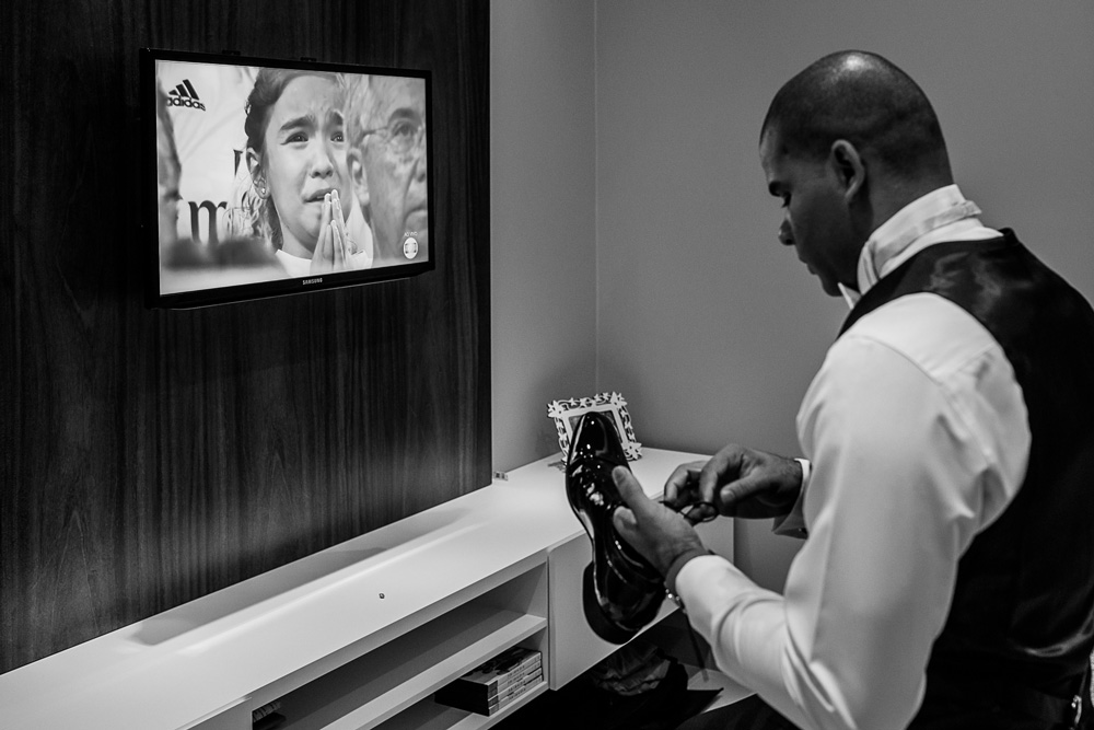 Noivo calçando o sapato enquanto uma menina rezava pelo seu time na tv