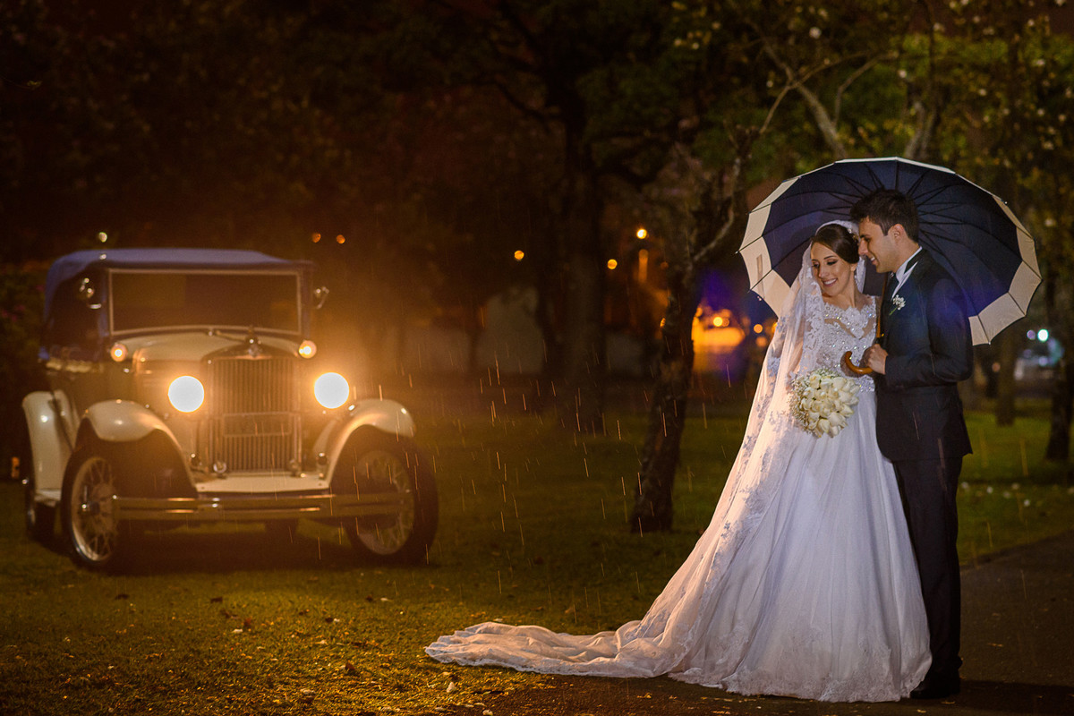 Ensaio dos noivos com carro antigo e sombrinha durante a chuva