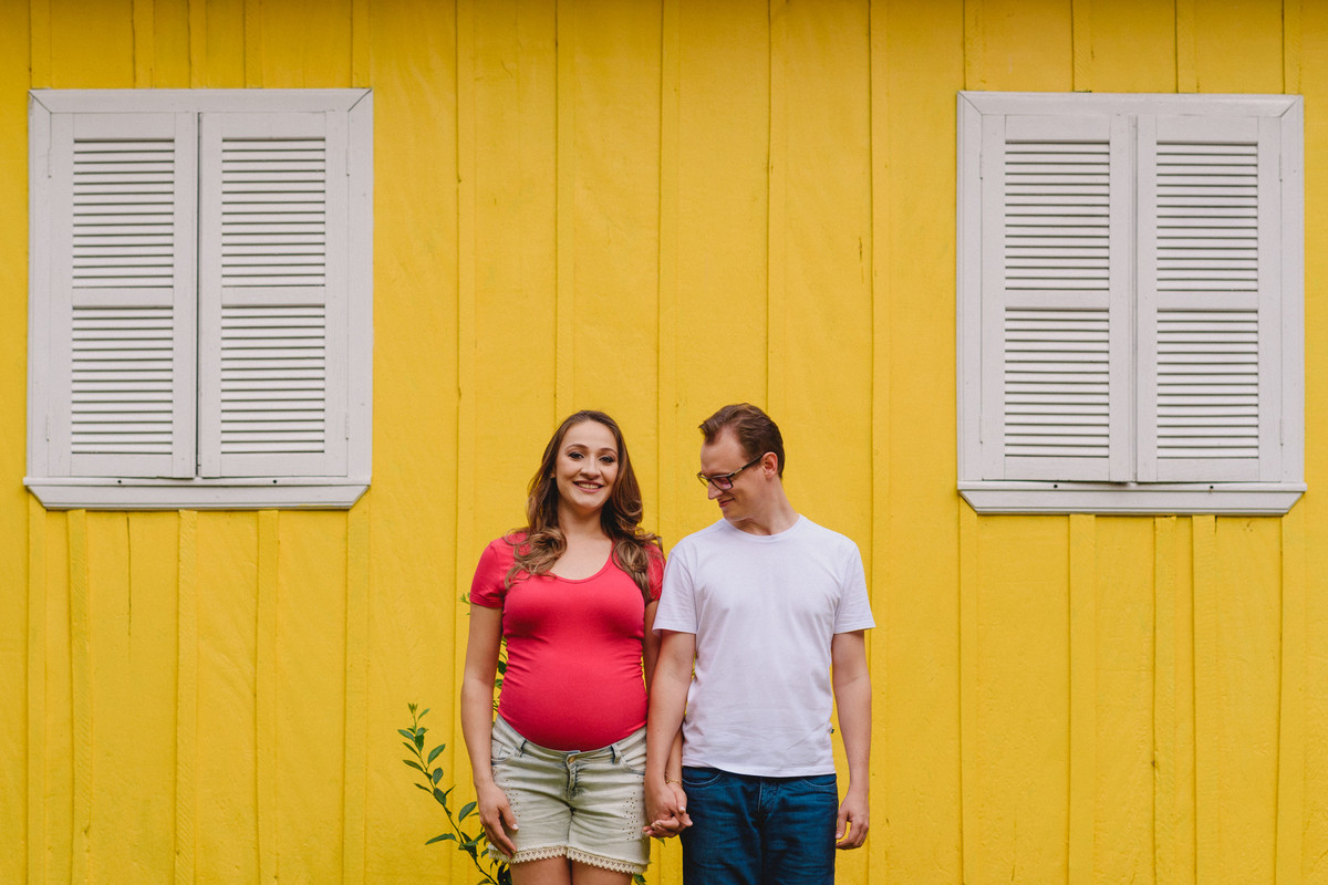 Ensaio de gestante, casal na frente de uma parede amarela