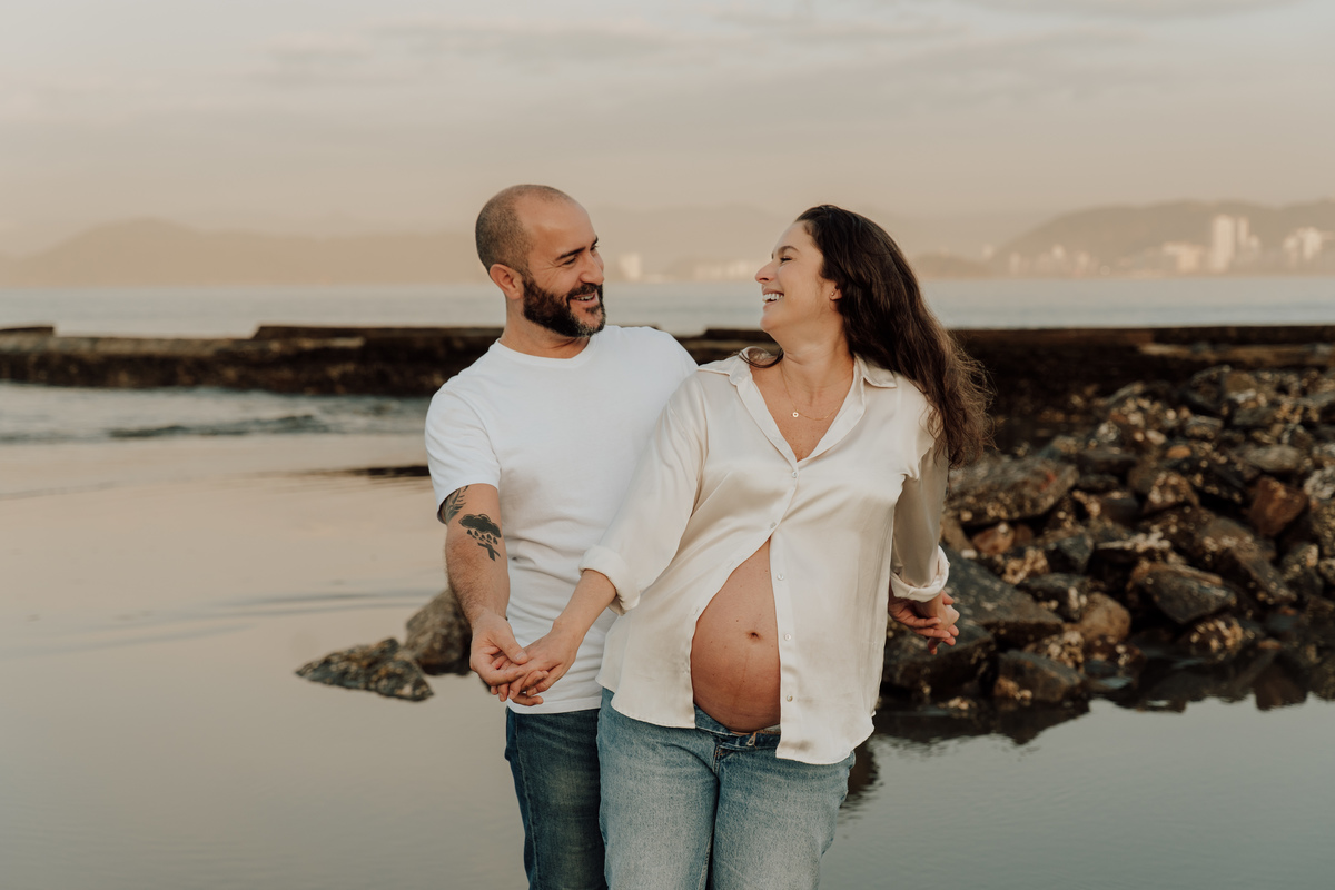 Fotografia de grávida na praia de Santos, usando calça jeans e camisa, capturando a tranquilidade da maternidade com luz natural suave. Foto ideal para ensaios de gestantes que buscam registros emocionantes da gravidez.