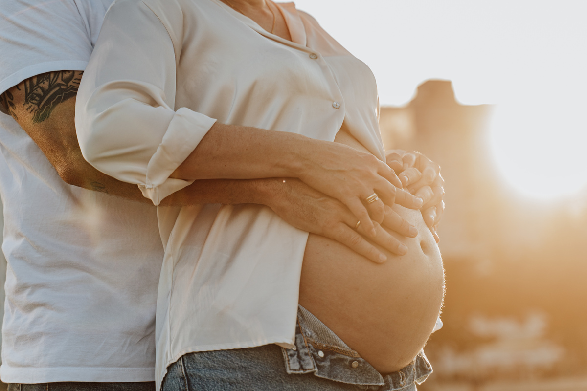 Fotografia de grávida na praia de Santos, usando calça jeans e camisa, capturando a tranquilidade da maternidade com luz natural suave. Foto ideal para ensaios de gestantes que buscam registros emocionantes da gravidez.