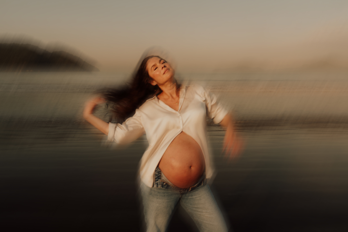 Fotografia de grávida na praia de Santos, usando calça jeans e camisa, capturando a tranquilidade da maternidade com luz natural suave. Foto ideal para ensaios de gestantes que buscam registros emocionantes da gravidez.