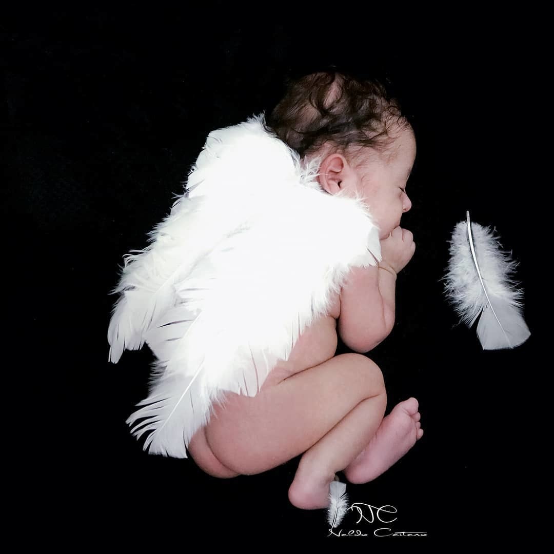 Ensaio fotógrafo  newbron anjinho o bebê está em uma manta preta e uma asa anjo branca na sua frente te um pena imagem linda fotógrafo Naldo Caitano Santos/SP